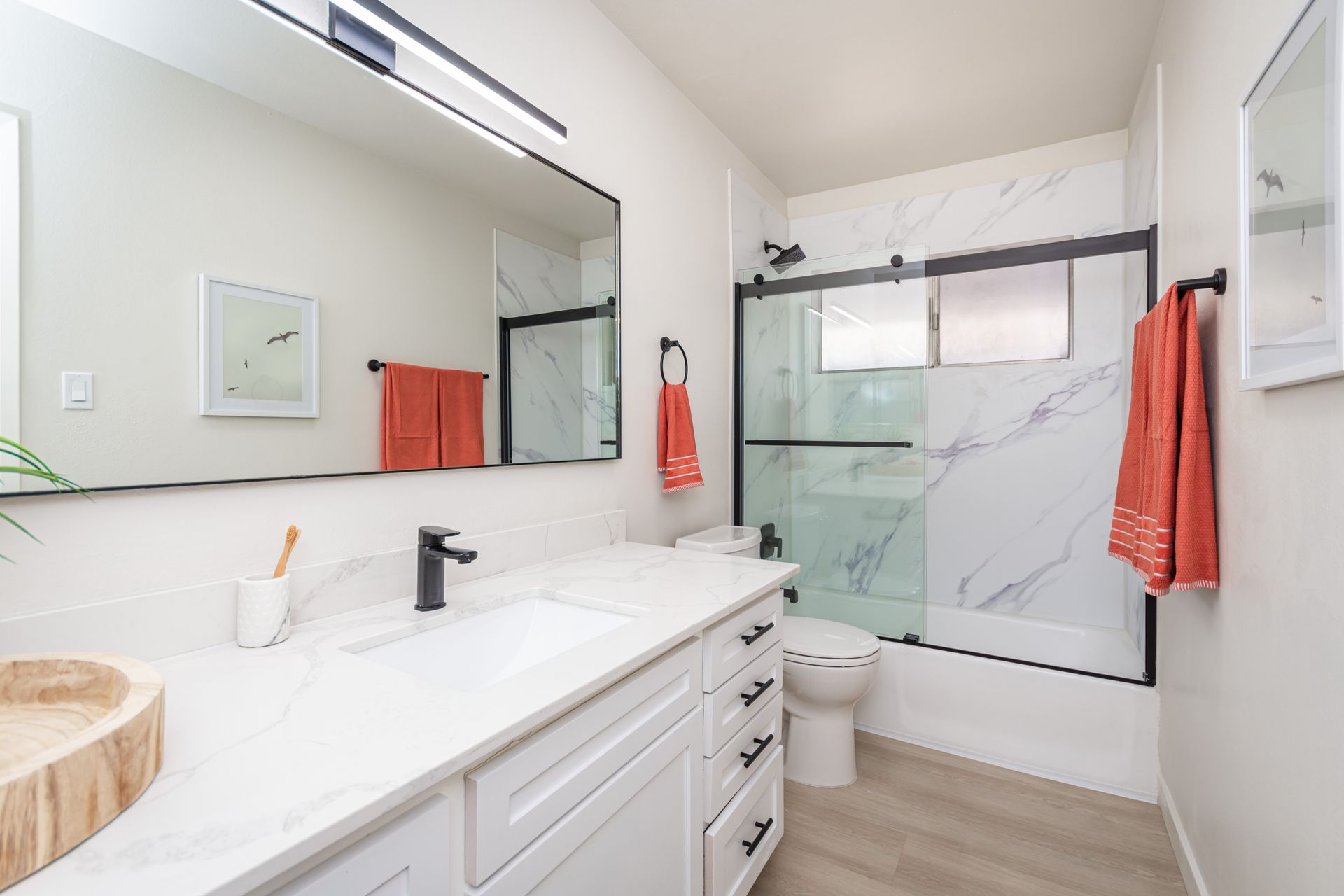 Bright modern bathroom with double vanity, large mirror, and glass shower with red towels