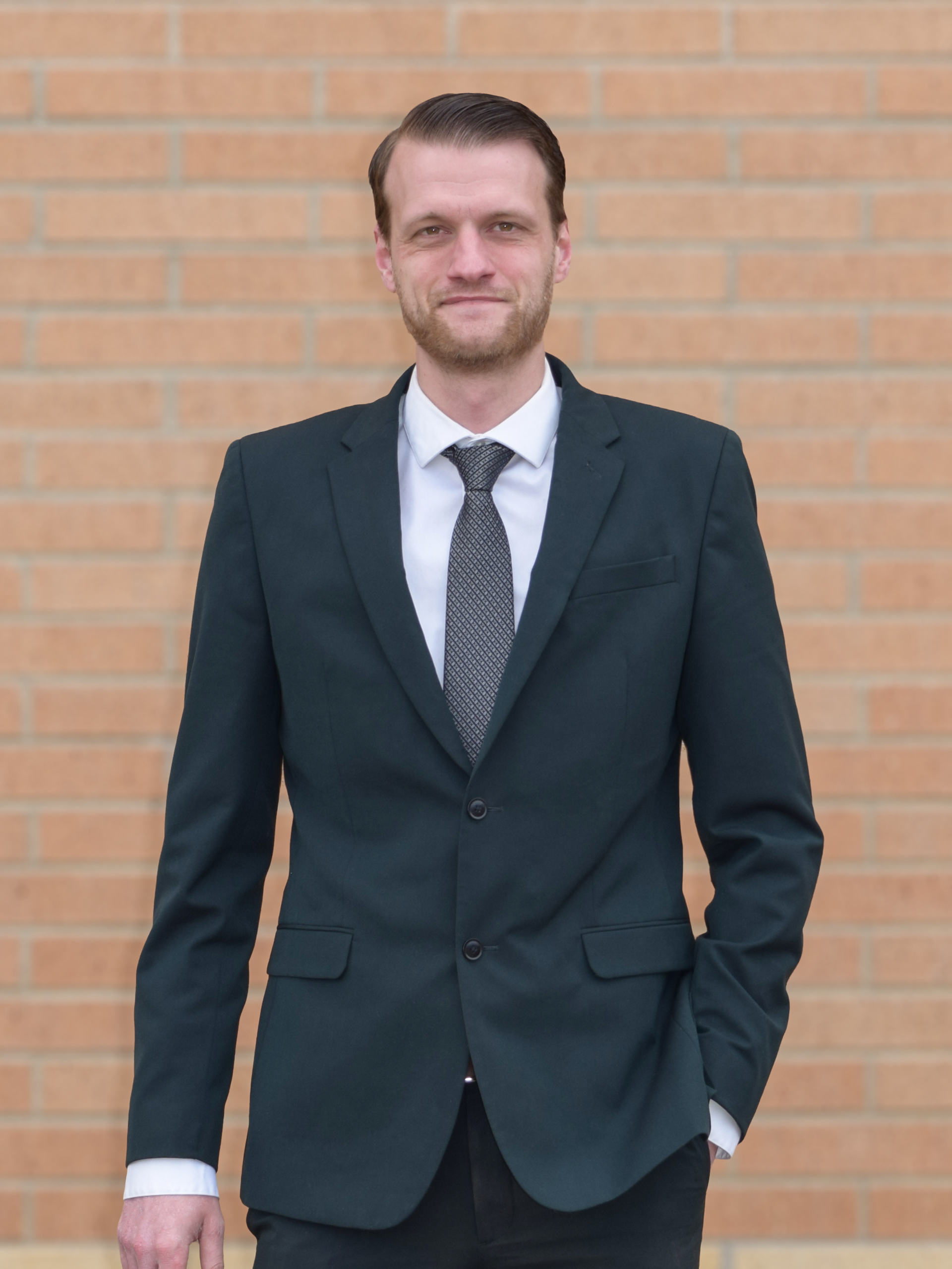Man in suit smiles in front of a wood-paneled wall with a company logo.