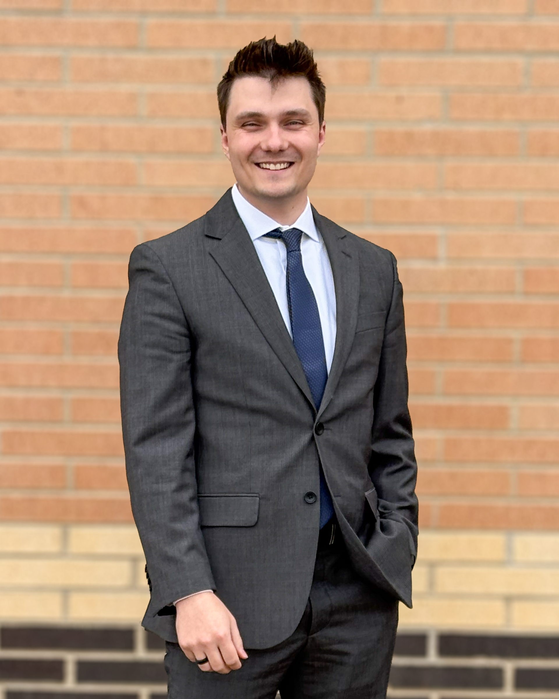 Man in suit smiles in front of a wood-paneled wall with a company logo.