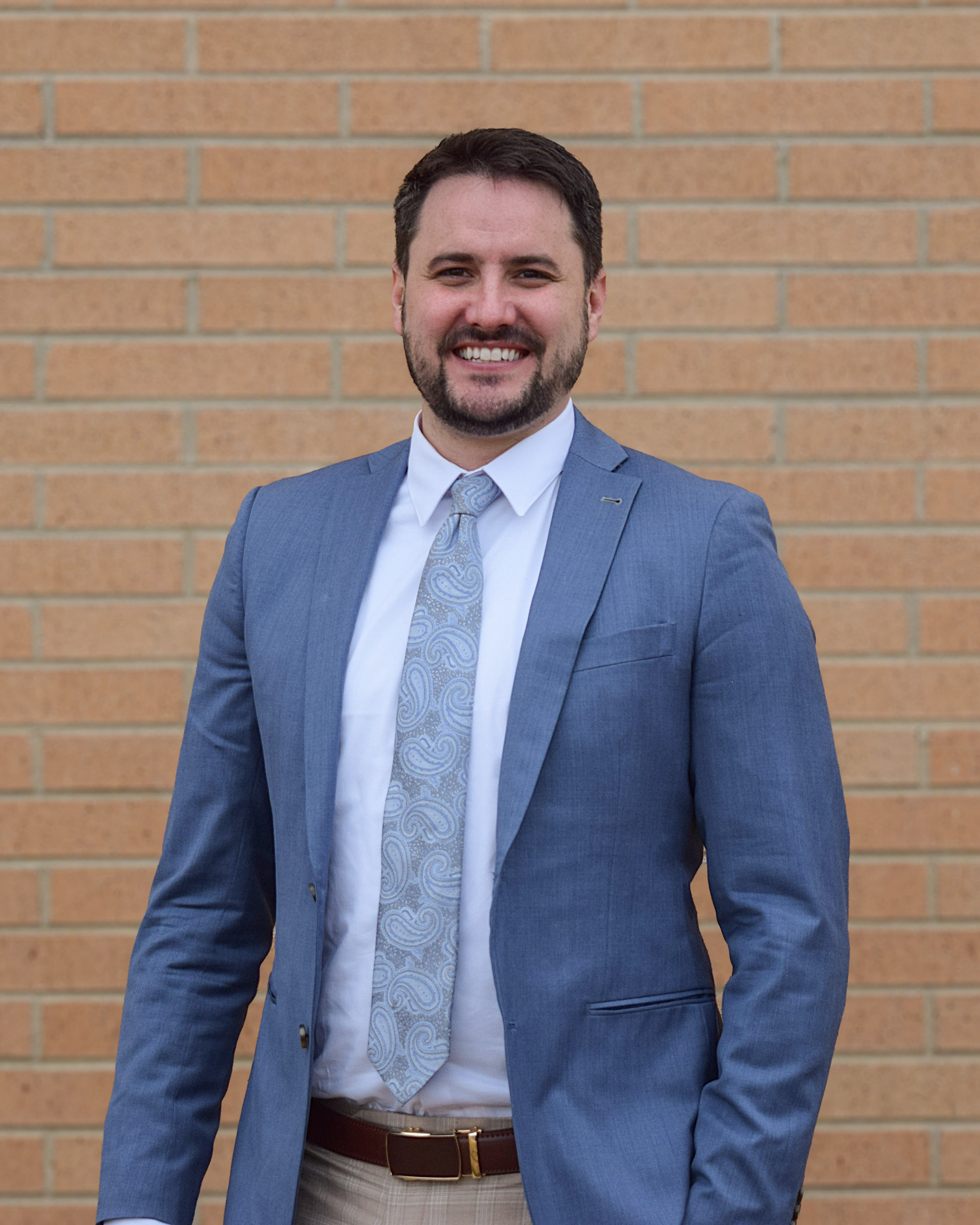 Man in suit smiles in front of a wood-paneled wall with a company logo.
