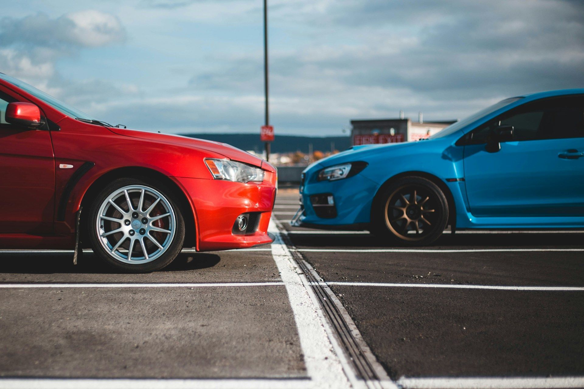 Red and blue sports cars face each other on a racetrack with a white center line.