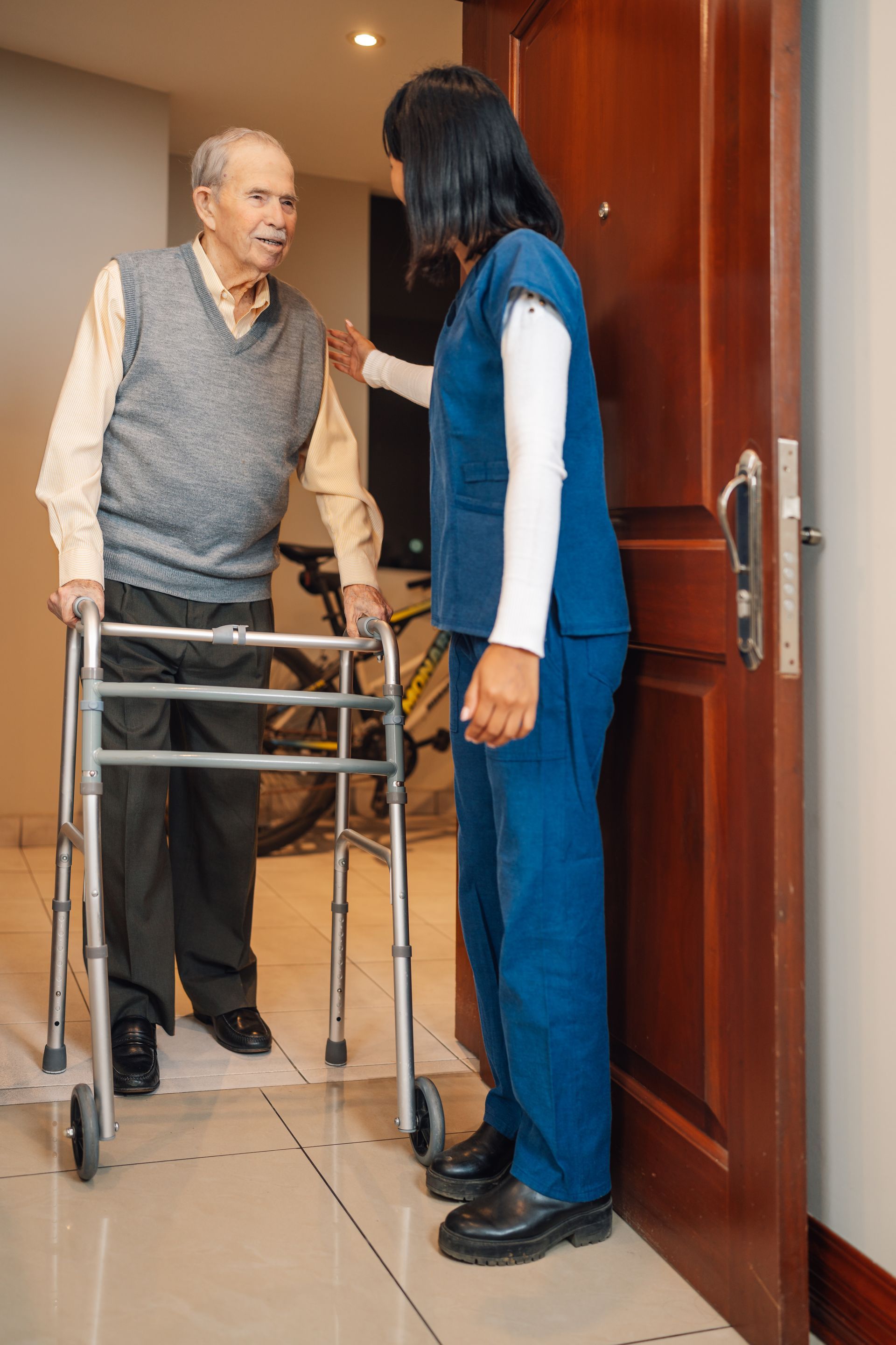 Woman assisting an elderly man with a walker in a doorway inside a home
