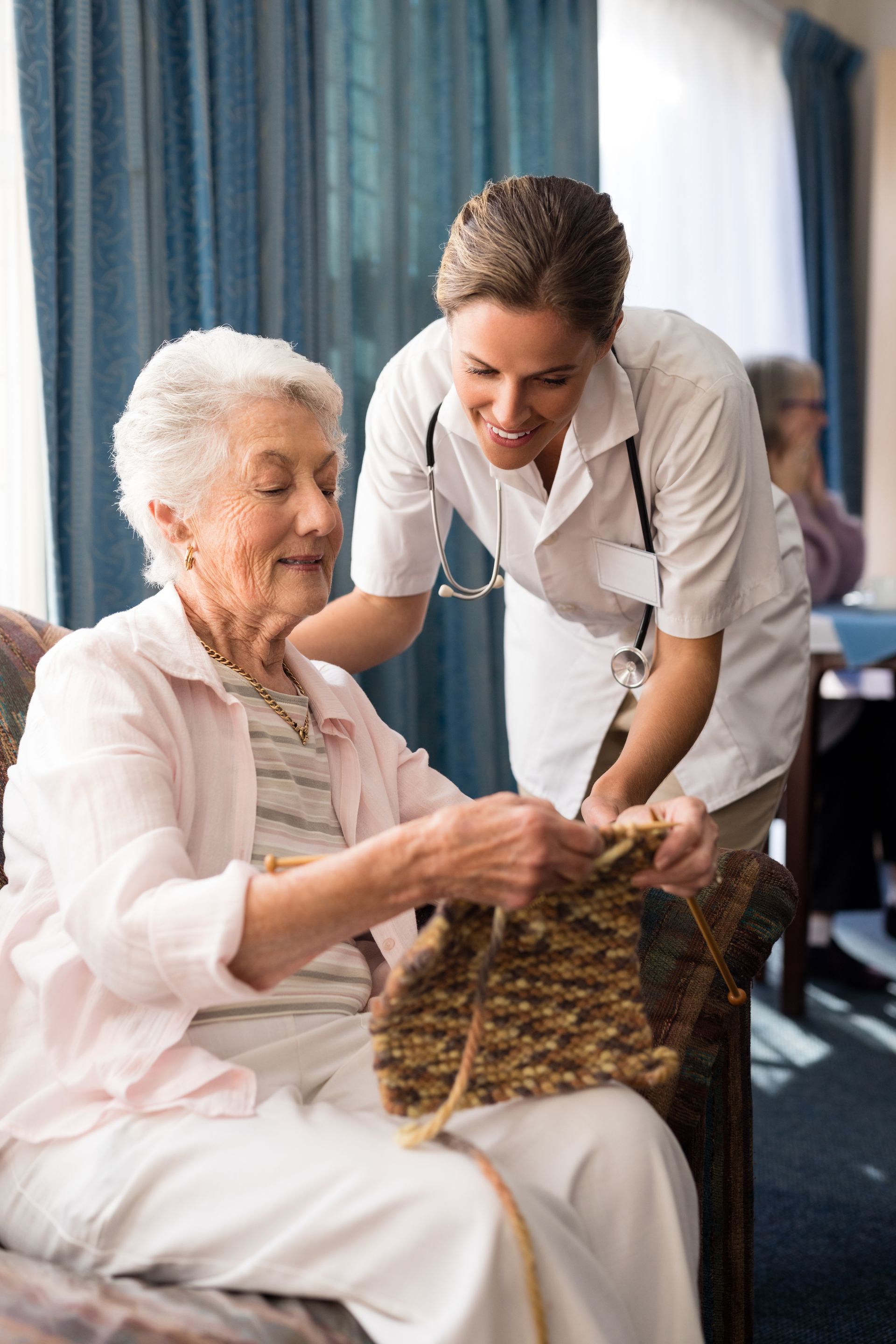 Caregiver helps elderly woman with woven basket in a bright room by the window