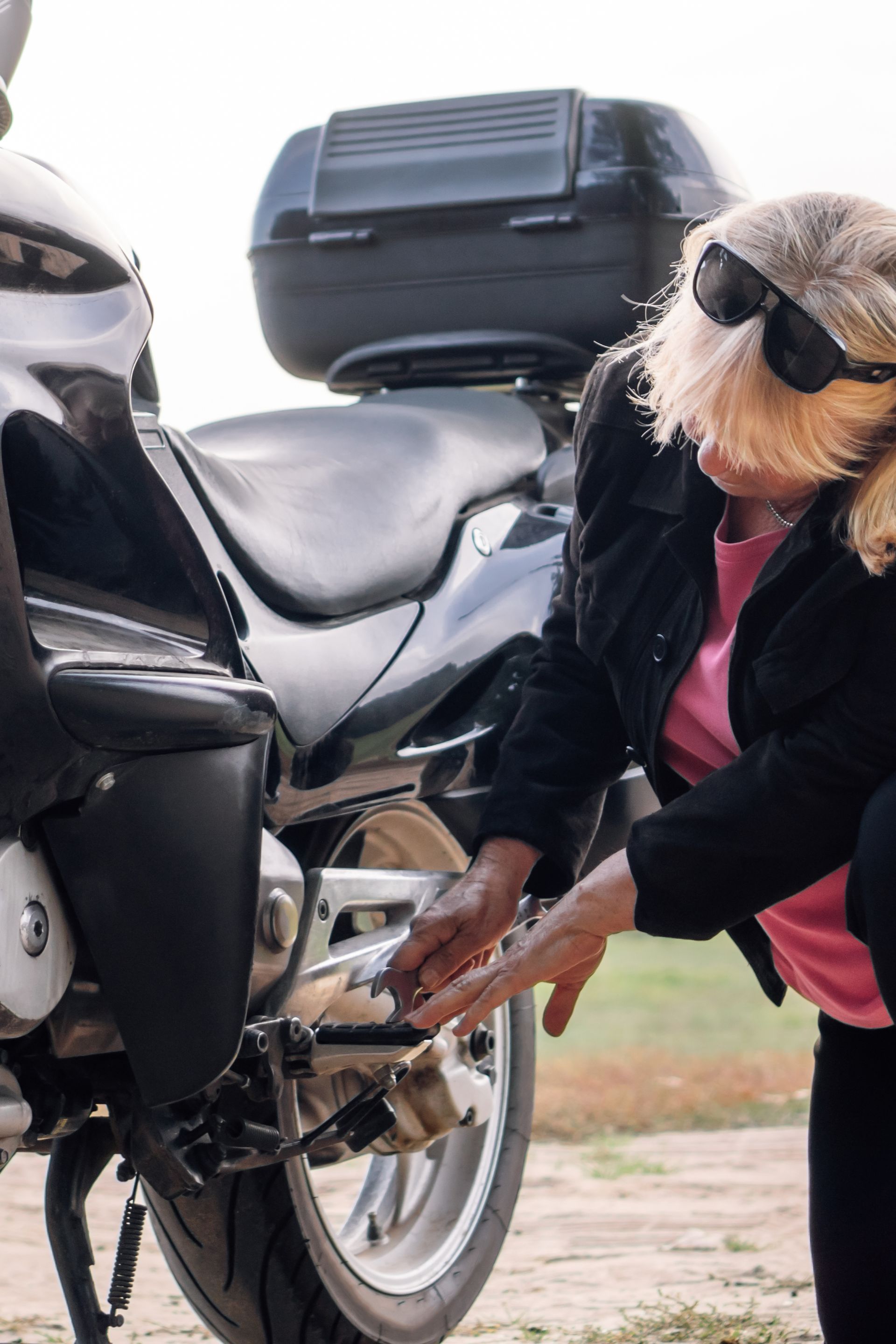 Person in sunglasses adjusts a motorcycle near luggage on a cobblestone road.
