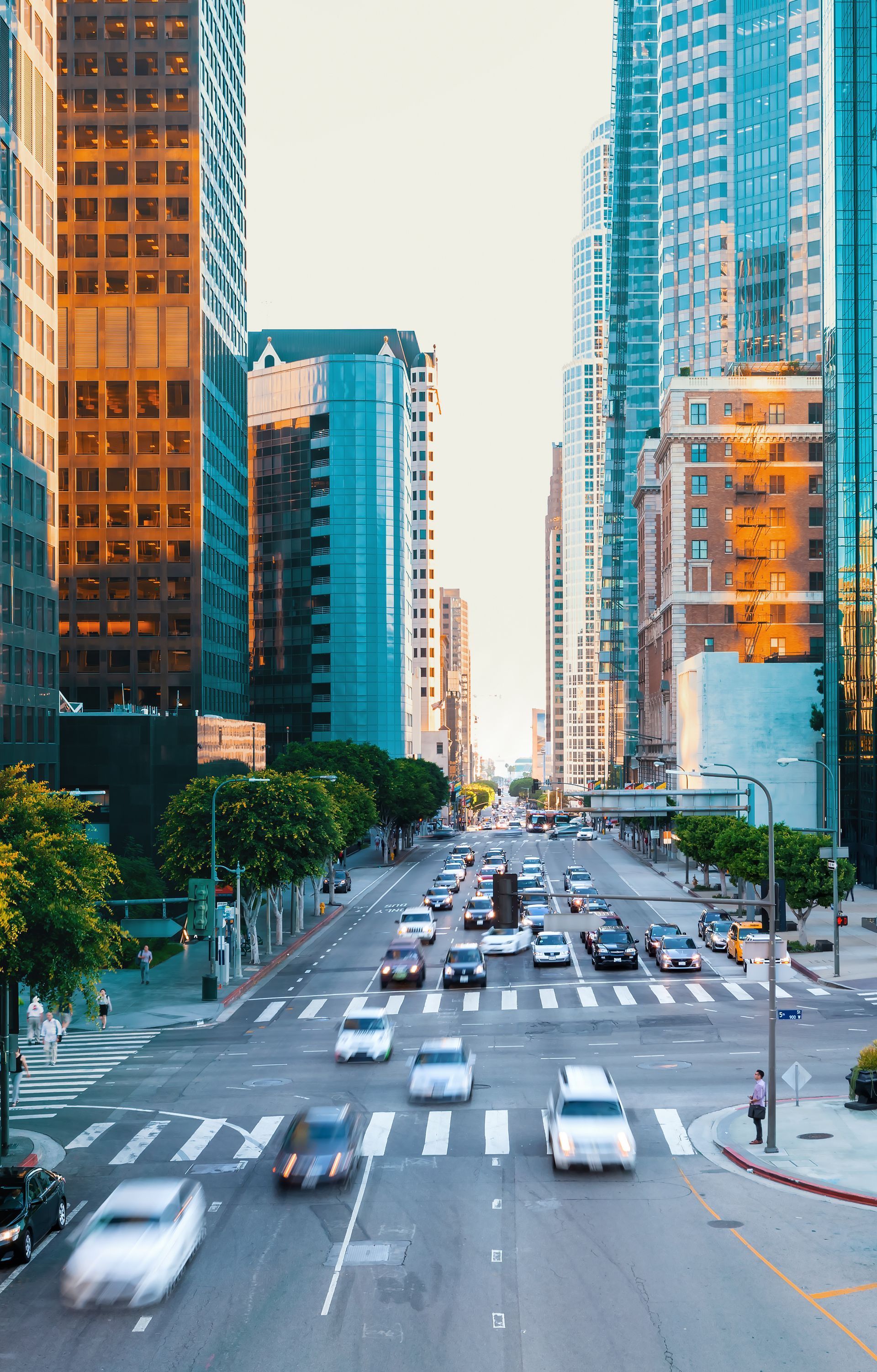 Busy city street between tall glass skyscrapers with cars driving in traffic