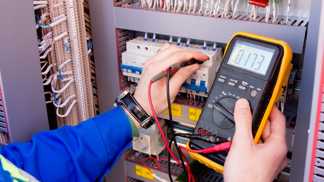 Technician using a multimeter to test wiring inside an electrical control panel