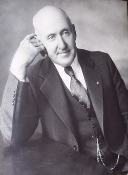 Black-and-white portrait of a smiling bald man in a suit, leaning his head on one hand.