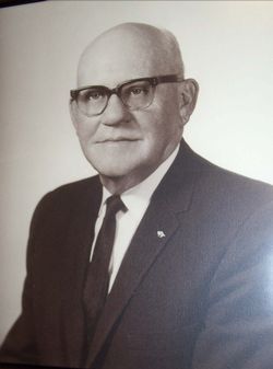 Portrait of a bald man in glasses and a suit, posed against a plain background.