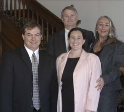Four people posing indoors on a staircase, dressed in formal attire, smiling at the camera.