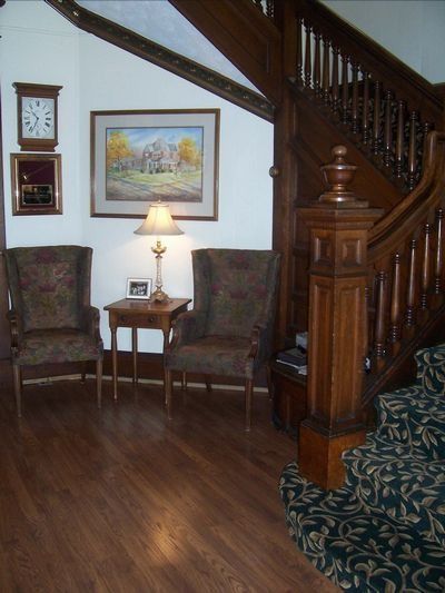 Cozy living room corner with two chairs, lamp, framed art, and wooden staircase.