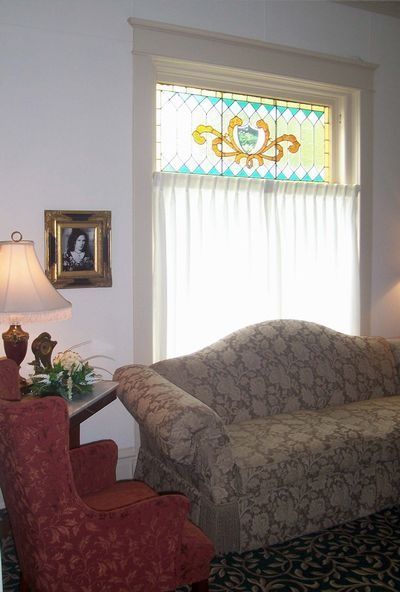 Living room with patterned sofa, red armchair, lamp, and stained-glass window above sheer curtains