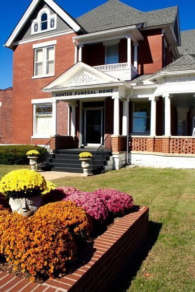 Brick house with white trim, front porch, and colorful flower beds in a sunny yard