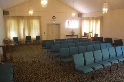 Empty meeting room with rows of blue chairs, curtained windows, and a closed door at the front.