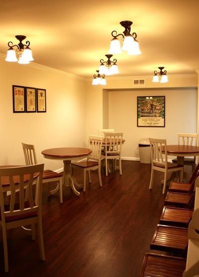 Empty cozy dining room with wooden tables, chairs, warm wall lights, and dark wood floor.