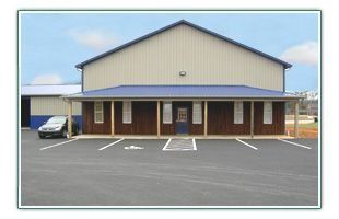 Small beige building with brown brick facade and empty parking lot in front