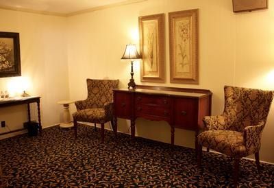 Quiet hotel room with patterned carpet, two armchairs, a wooden desk, and wall lamps.