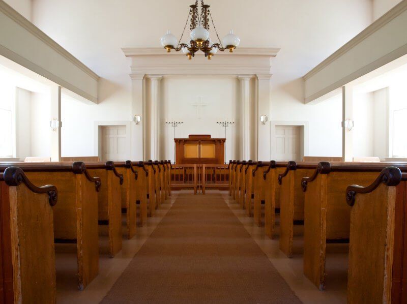 An empty church with wooden benches and a chandelier hanging from the ceiling