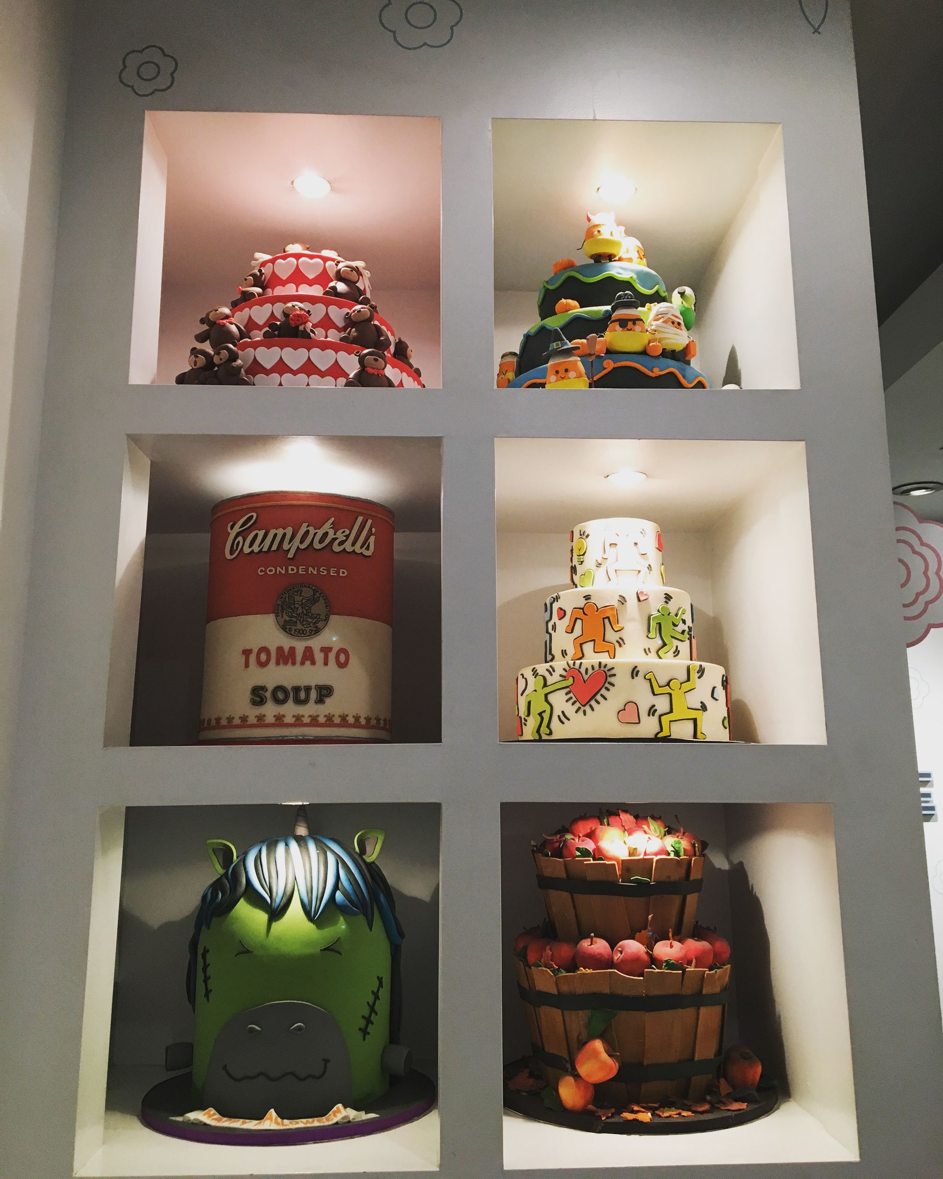 Display of colorful decorative cakes in lit cubby holes.
