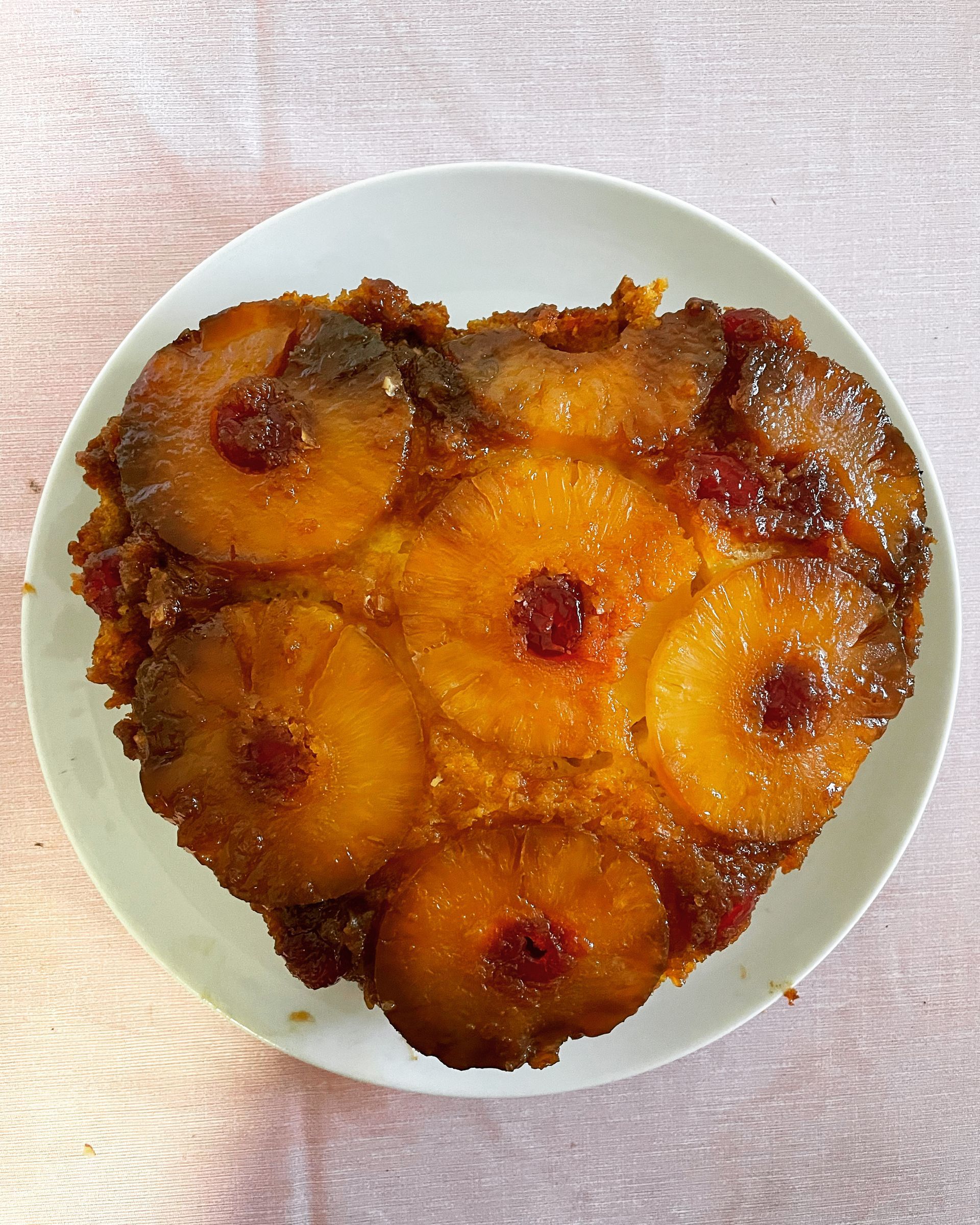 Pineapple upside-down cake on a white plate, with pineapple rings and cherries visible.