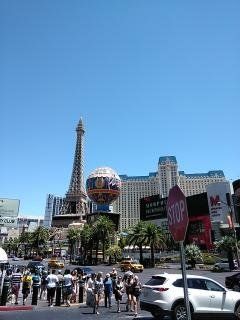 Las Vegas Strip: Eiffel Tower replica, globe, stop sign, cars, people, and clear blue sky.