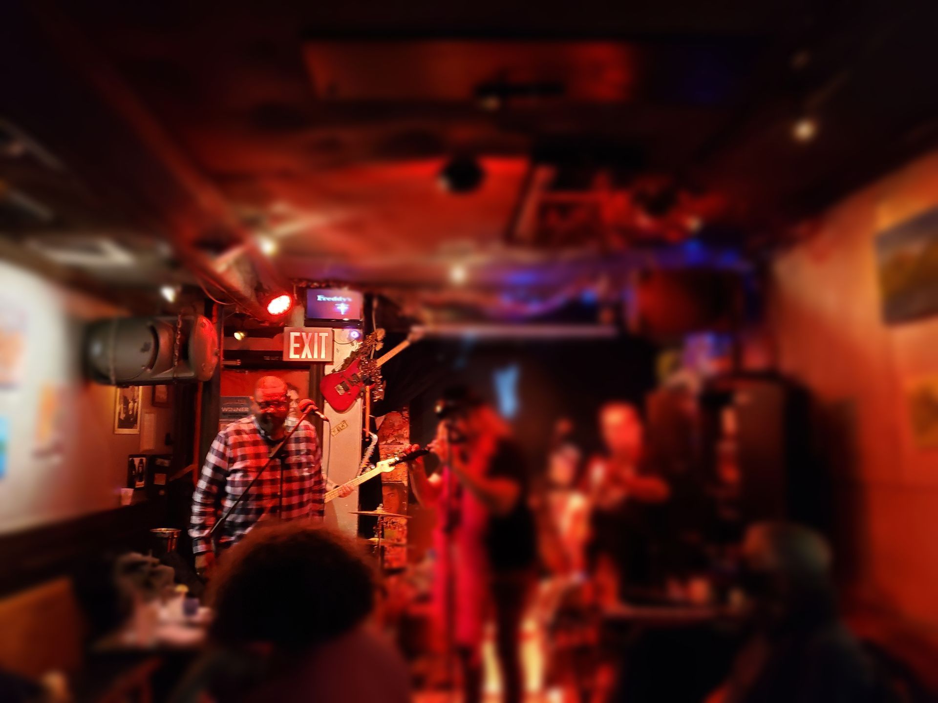 Band performing in a dimly lit bar, red and blue stage lighting, audience watching.