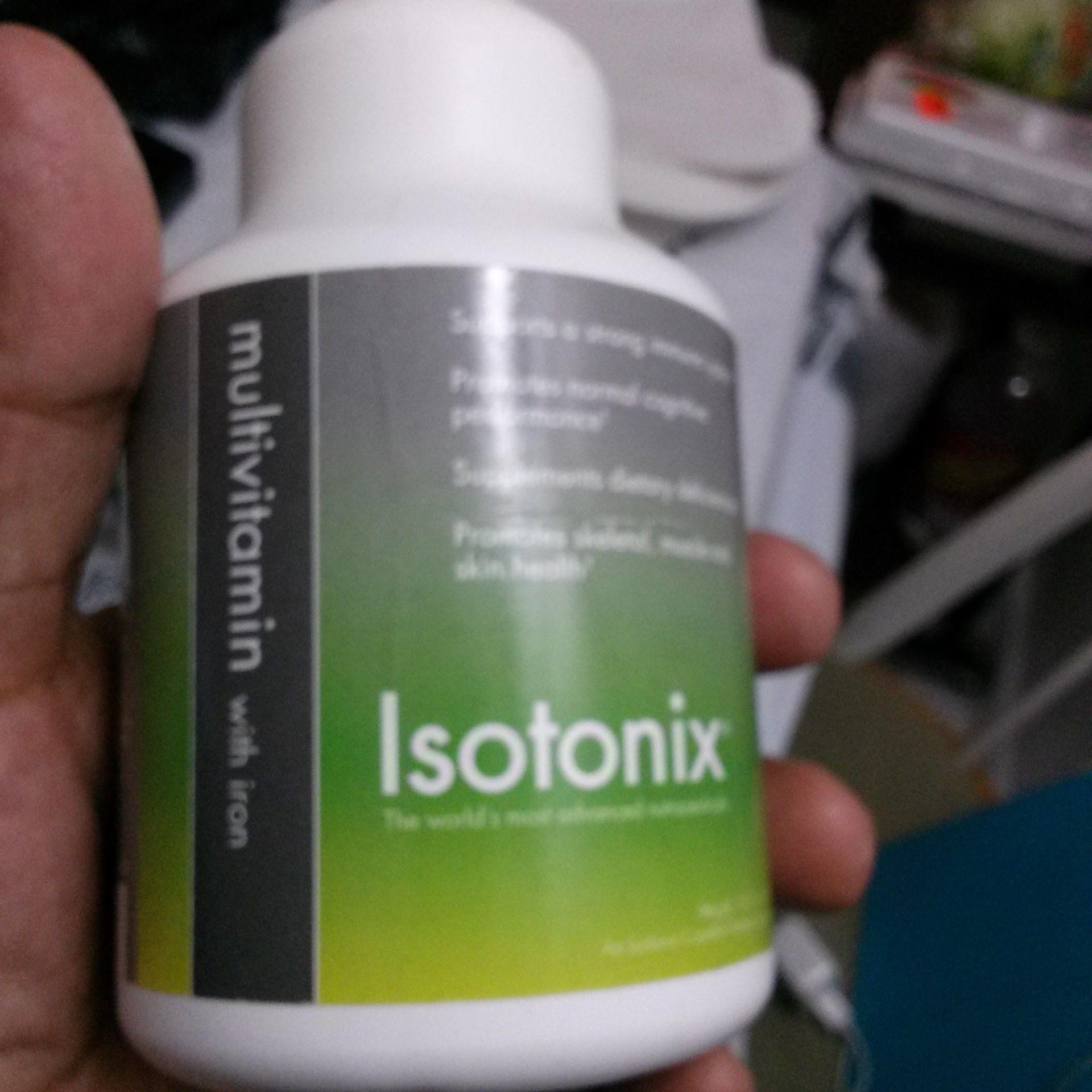 A person holds a white bottle of Isotonix multivitamin with iron. The label is white, gray, and green.