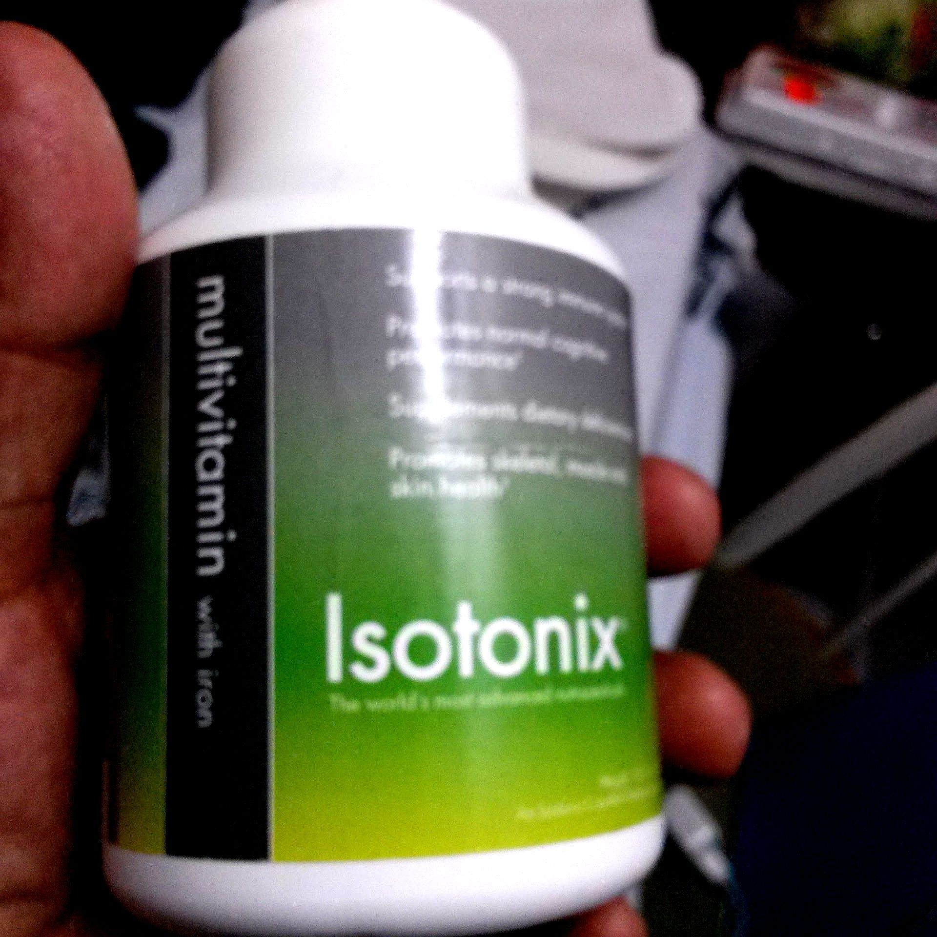 A hand holding a white bottle of Isotonix multivitamin with a green and gray label.