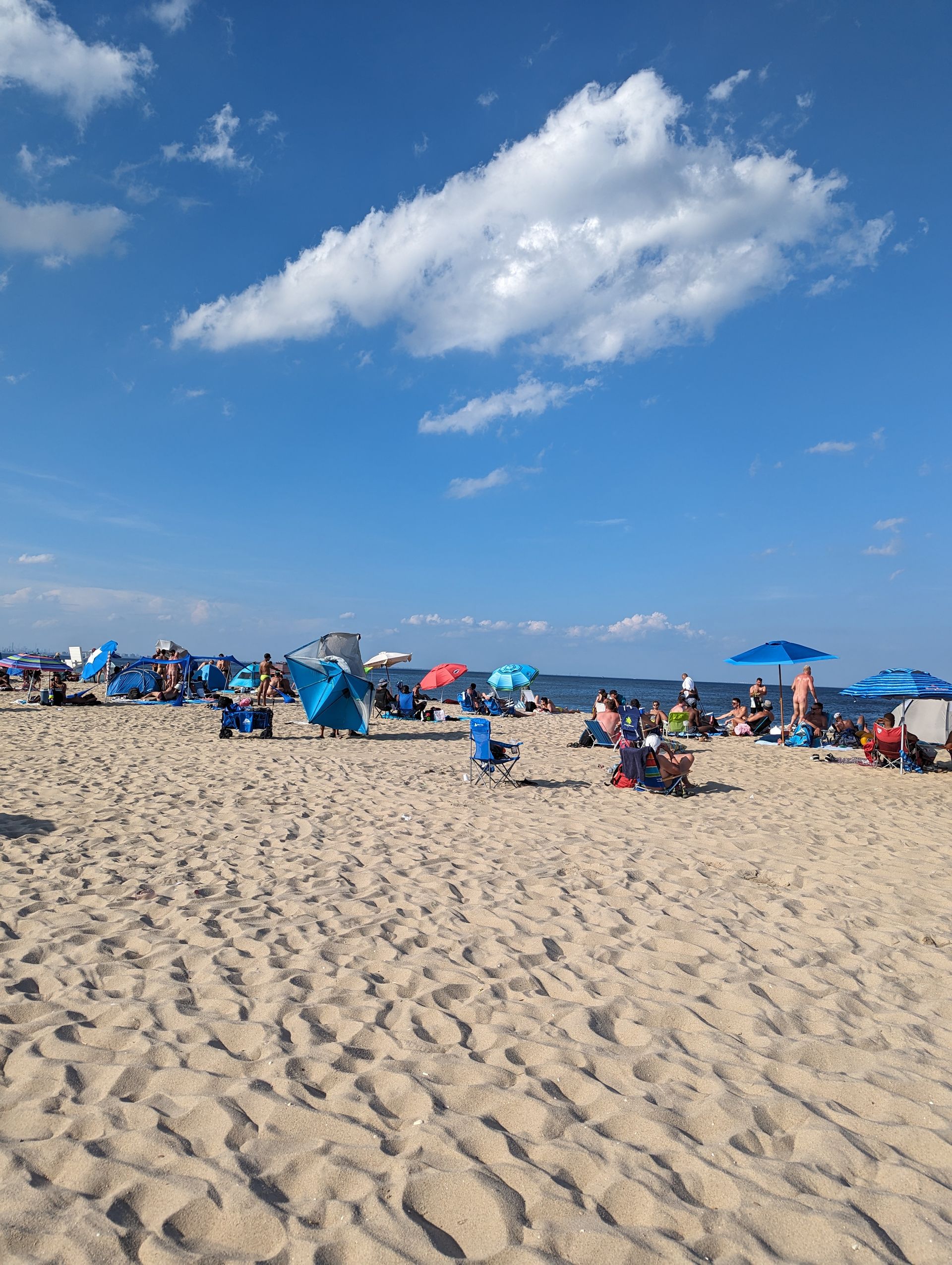 Sandy beach with people relaxing under umbrellas on a sunny day. Blue sky, white clouds.