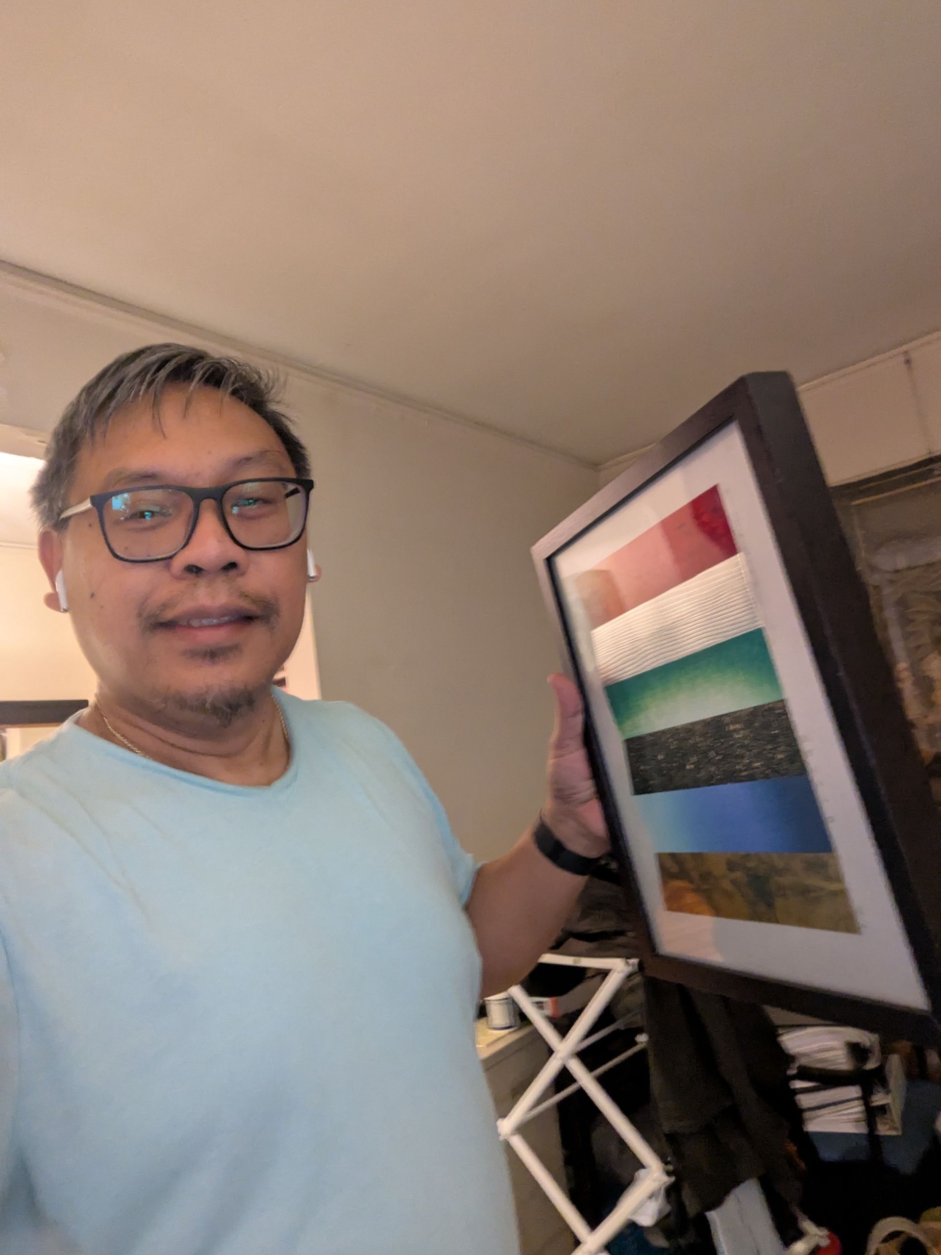 Man in blue shirt holding a framed abstract art piece with colorful horizontal bands.