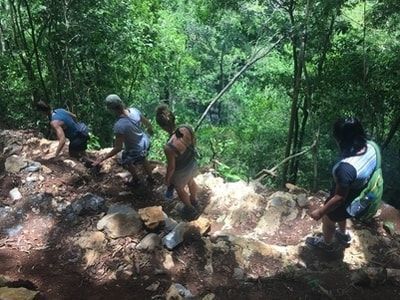 Missionaries on a trail in the woods with cliff on the side of trail