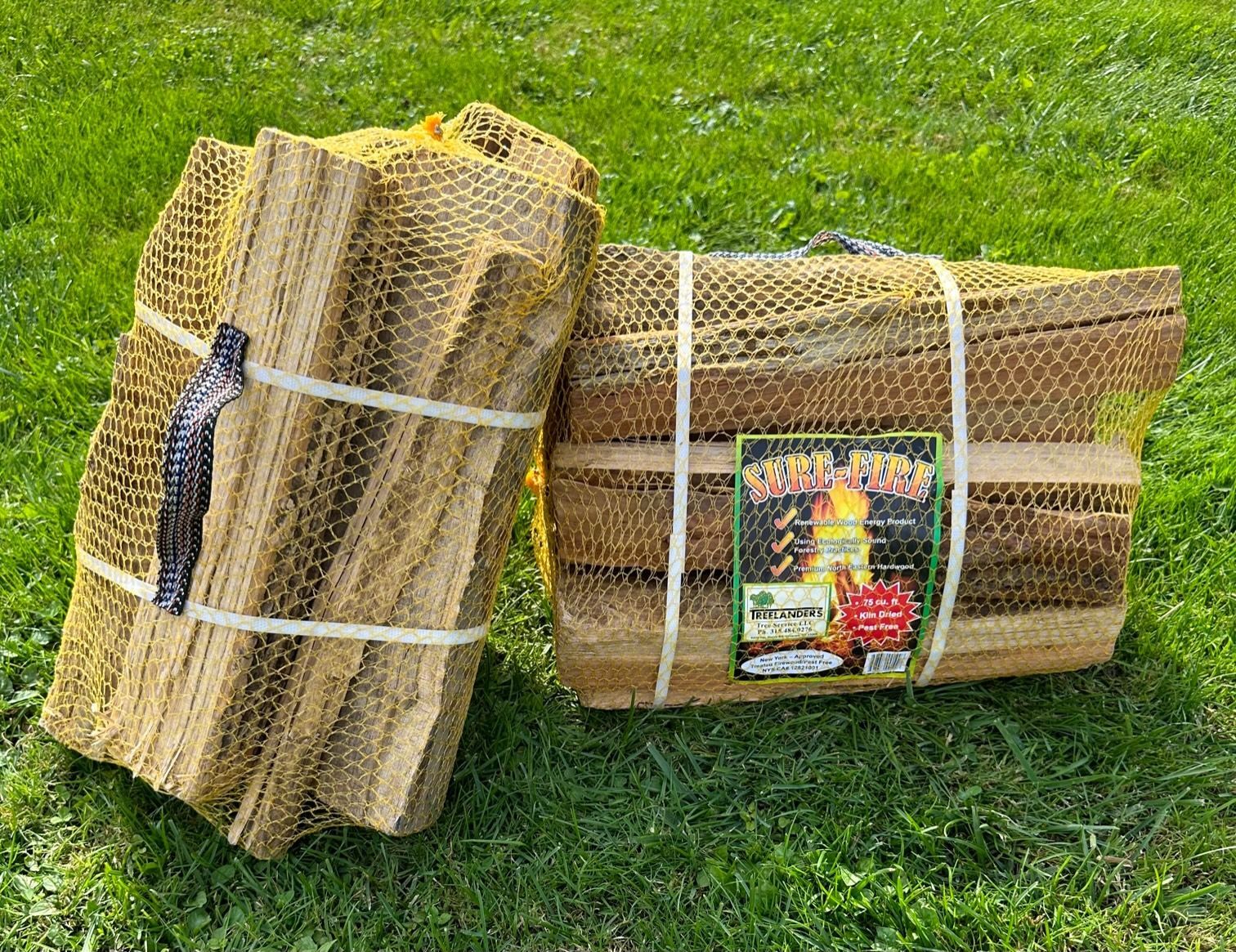 Two bundles of firewood in mesh bags, on a grassy lawn.