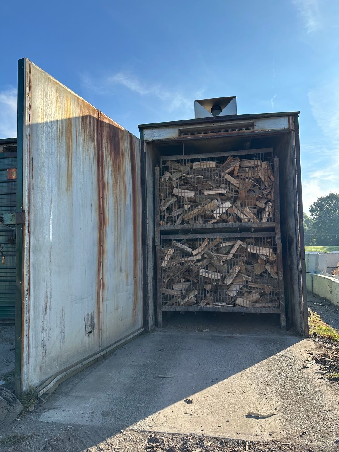 Open kiln with two metal crates of firewood, weathered metal, outdoor setting.