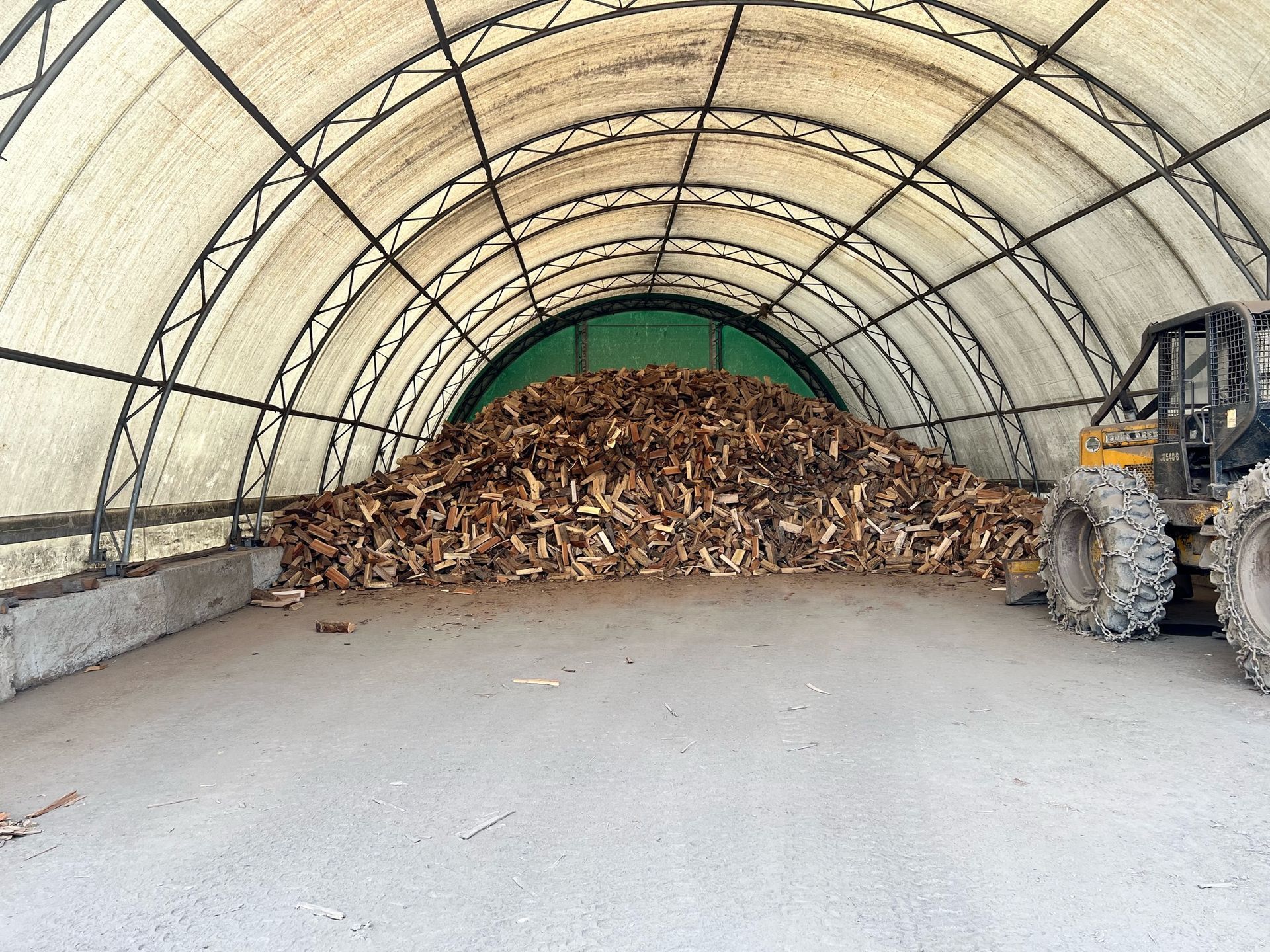 Pile of wood chips inside a large arched structure with a piece of heavy machinery on the right.
