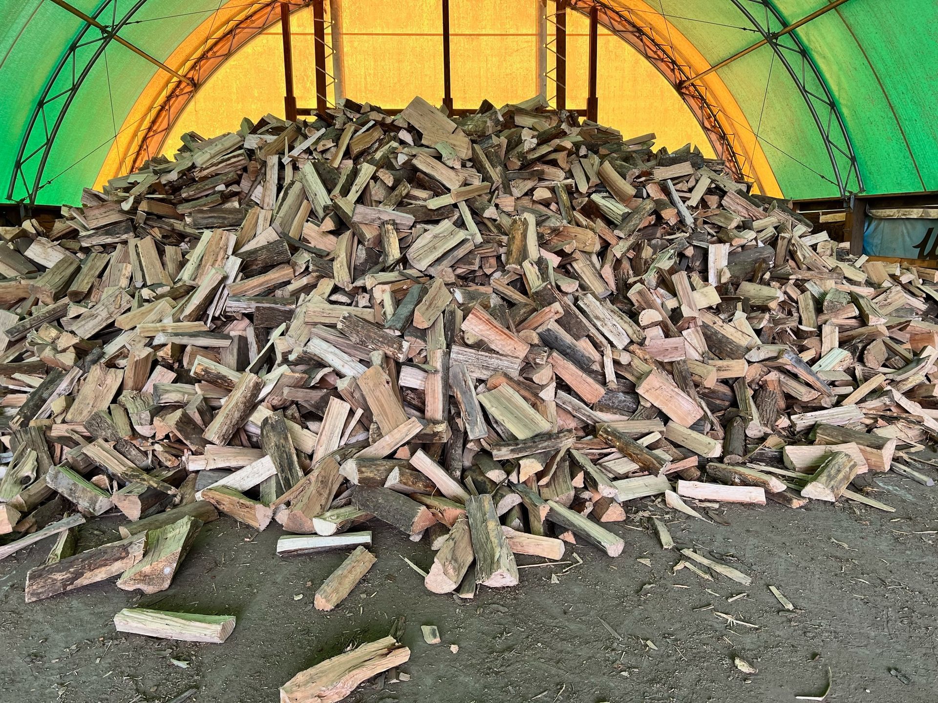 Pile of split firewood inside a yellow-roofed shelter.