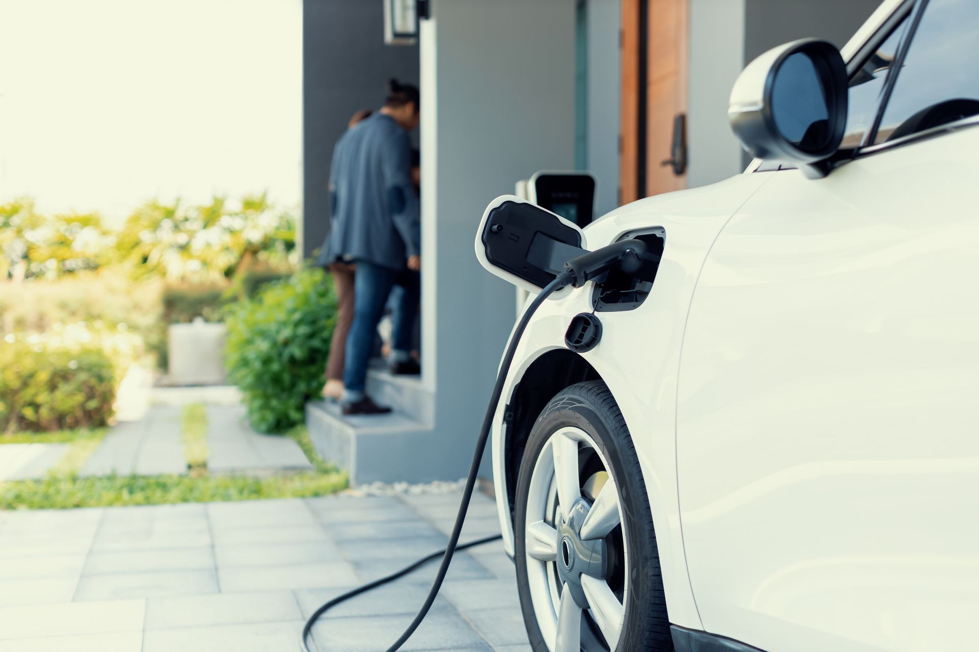A white electric car is being charged in front of a house.