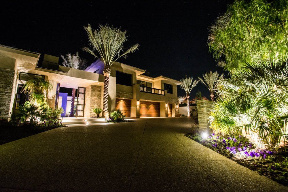 A large house is lit up at night with palm trees in front of it.