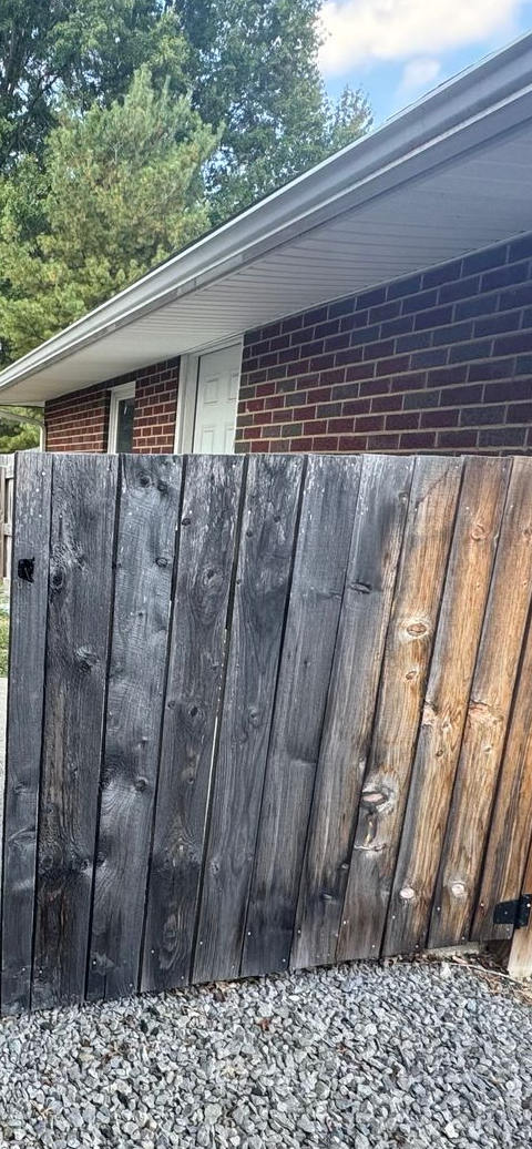 A weathered wooden fence in front of a brick building with a white eave and a door.