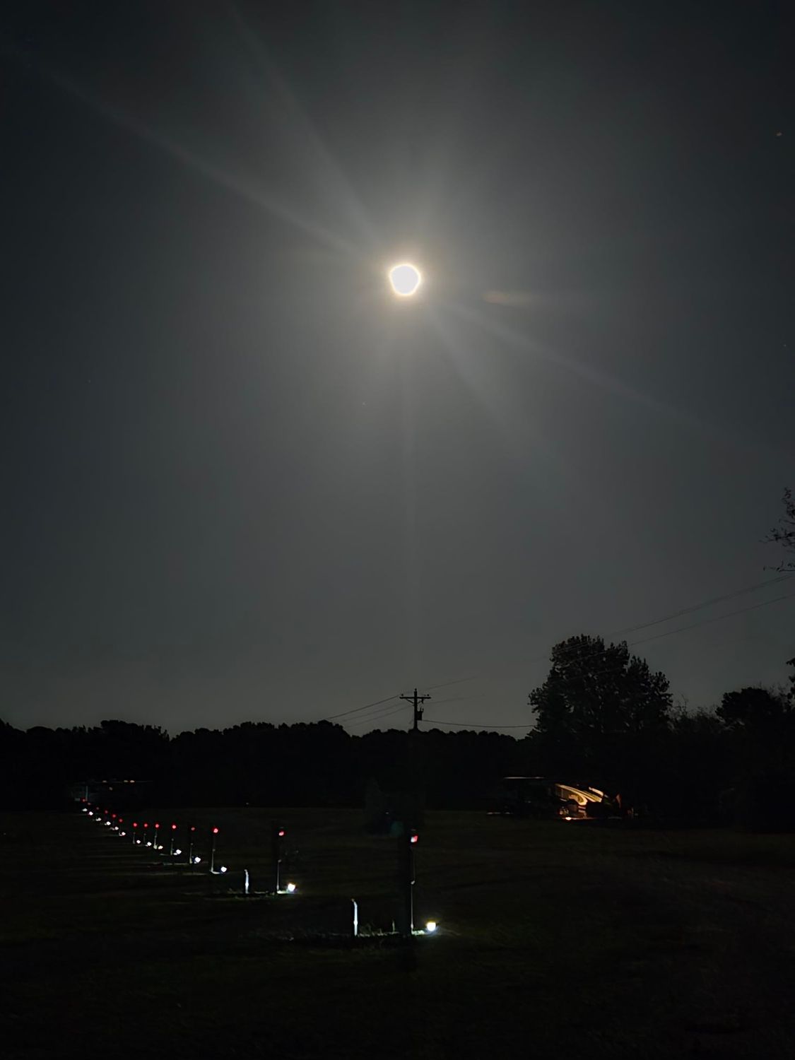 Full moon shining brightly above a dark field with line of lights.