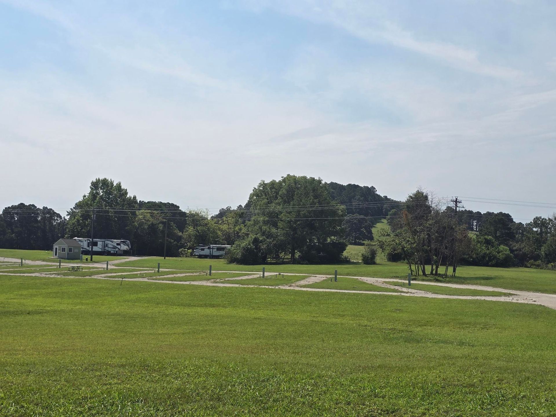 Grassy park with a winding path, trees, and a few parked cars under a clear sky