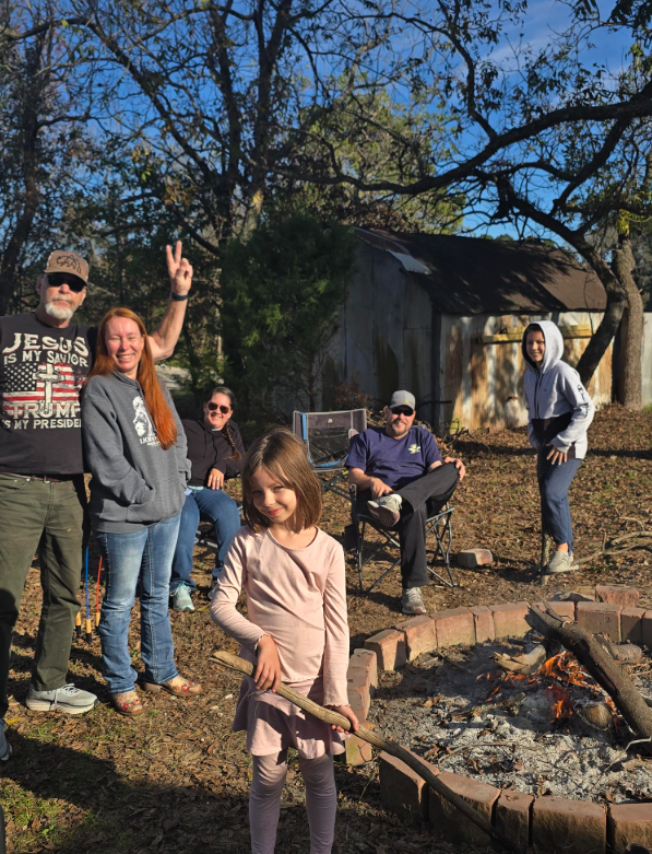 People gathered around a backyard fire pit, with one child holding a stick over the flames.