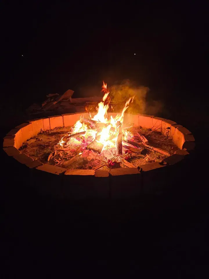 A small campfire burning in a circular fire pit at night
