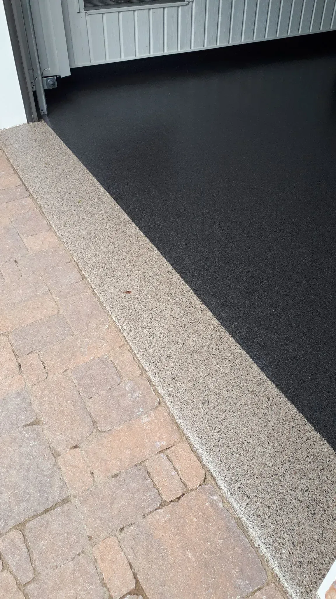 Garage entrance with black epoxy floor, tan border, and brick driveway.