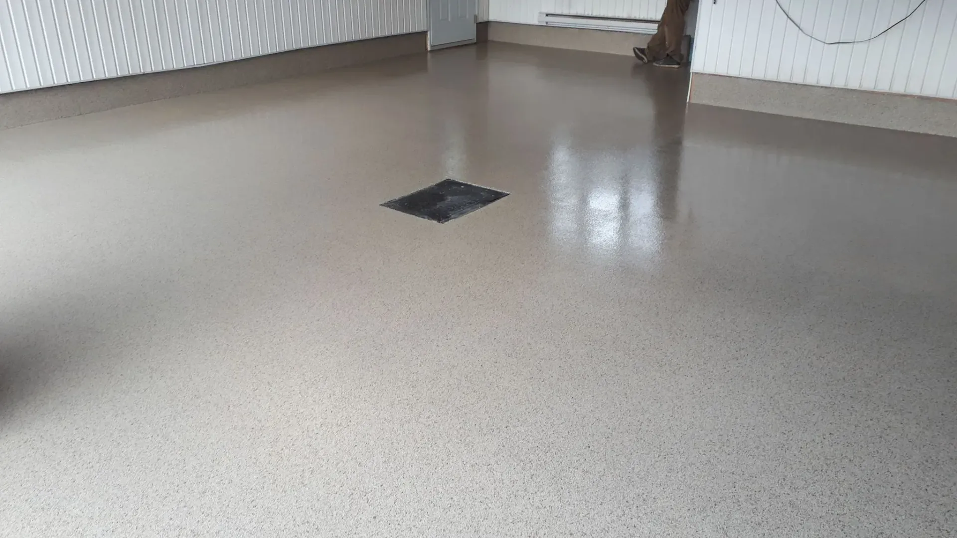 Epoxy-coated floor with speckled aggregate. Gray surface, black drain, white textured walls.