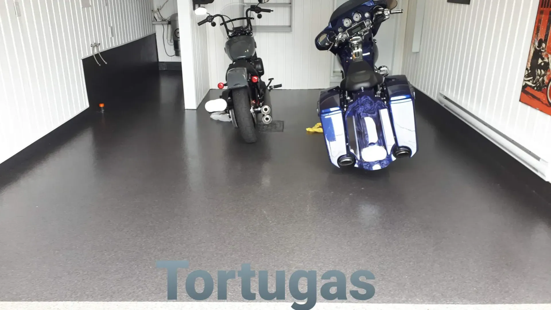 Two motorcycles parked inside a garage. Black and white walls, dark gray flooring. 
