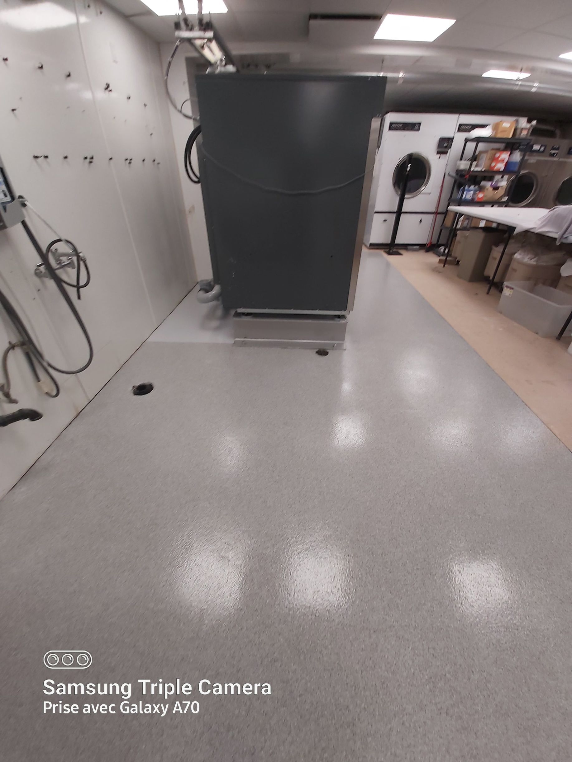 A commercial laundry room with a large gray machine centered on a light gray floor.