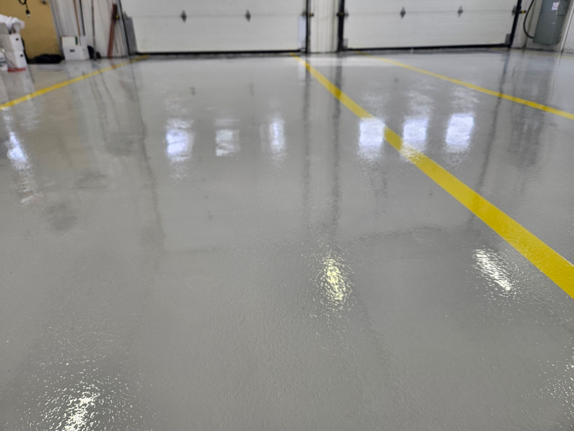 Gray epoxy floor with yellow lines in a garage setting, reflecting overhead lights.
