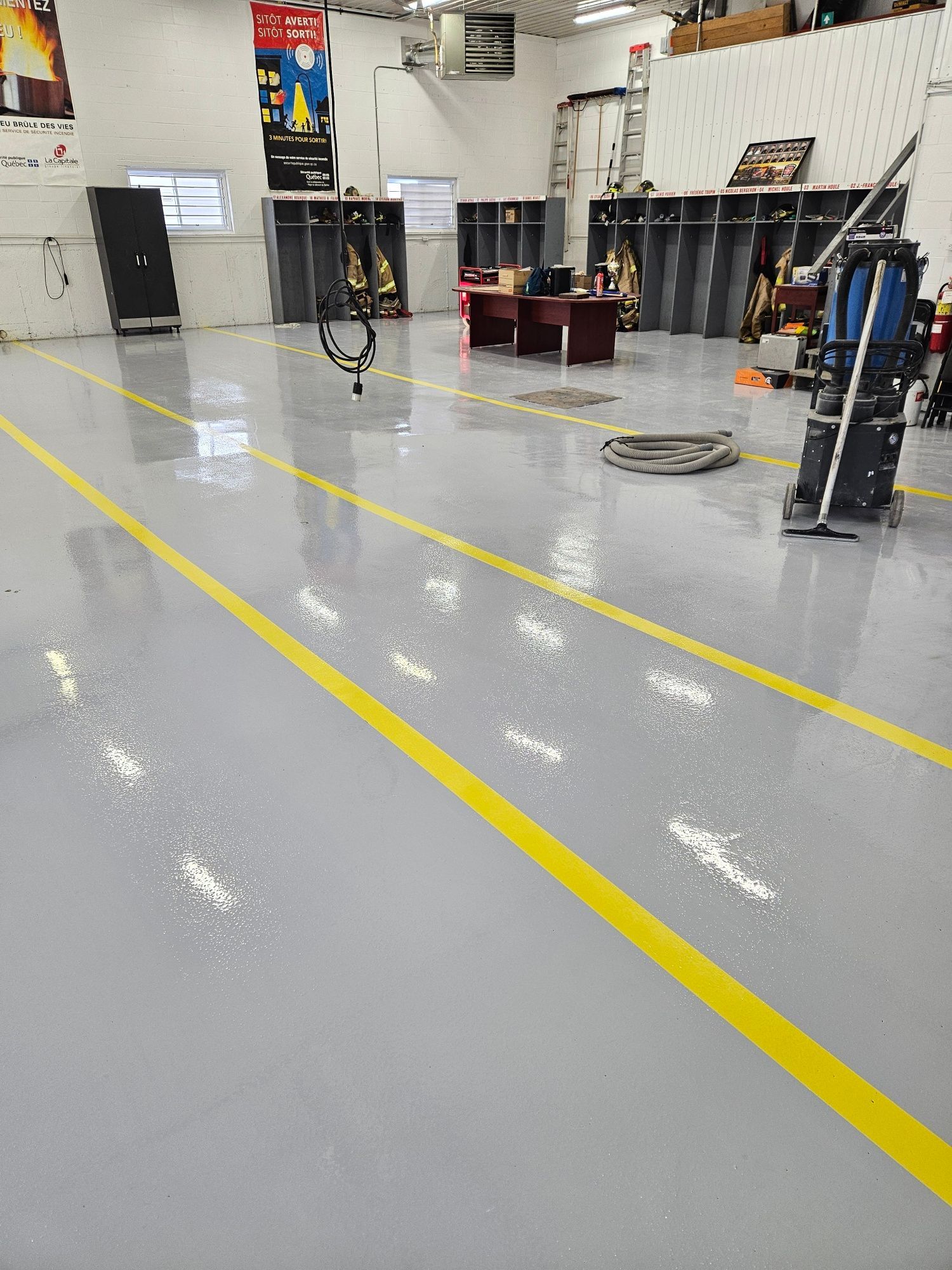 Interior of a fire station with a newly cleaned gray floor and yellow lines. Equipment and furniture are present.
