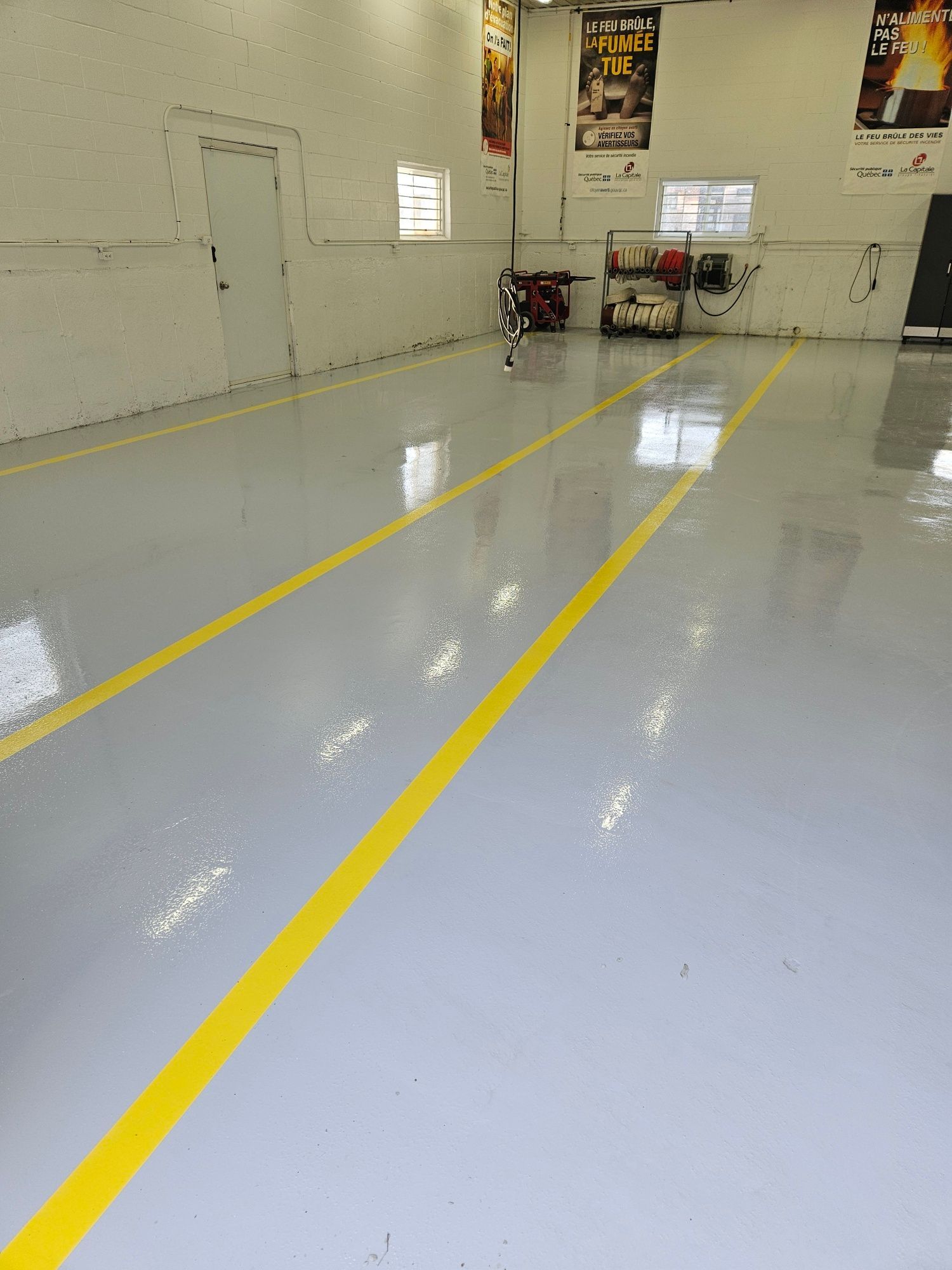 Yellow lines on a shiny gray floor in a large white room. Equipment and posters are along the wall.