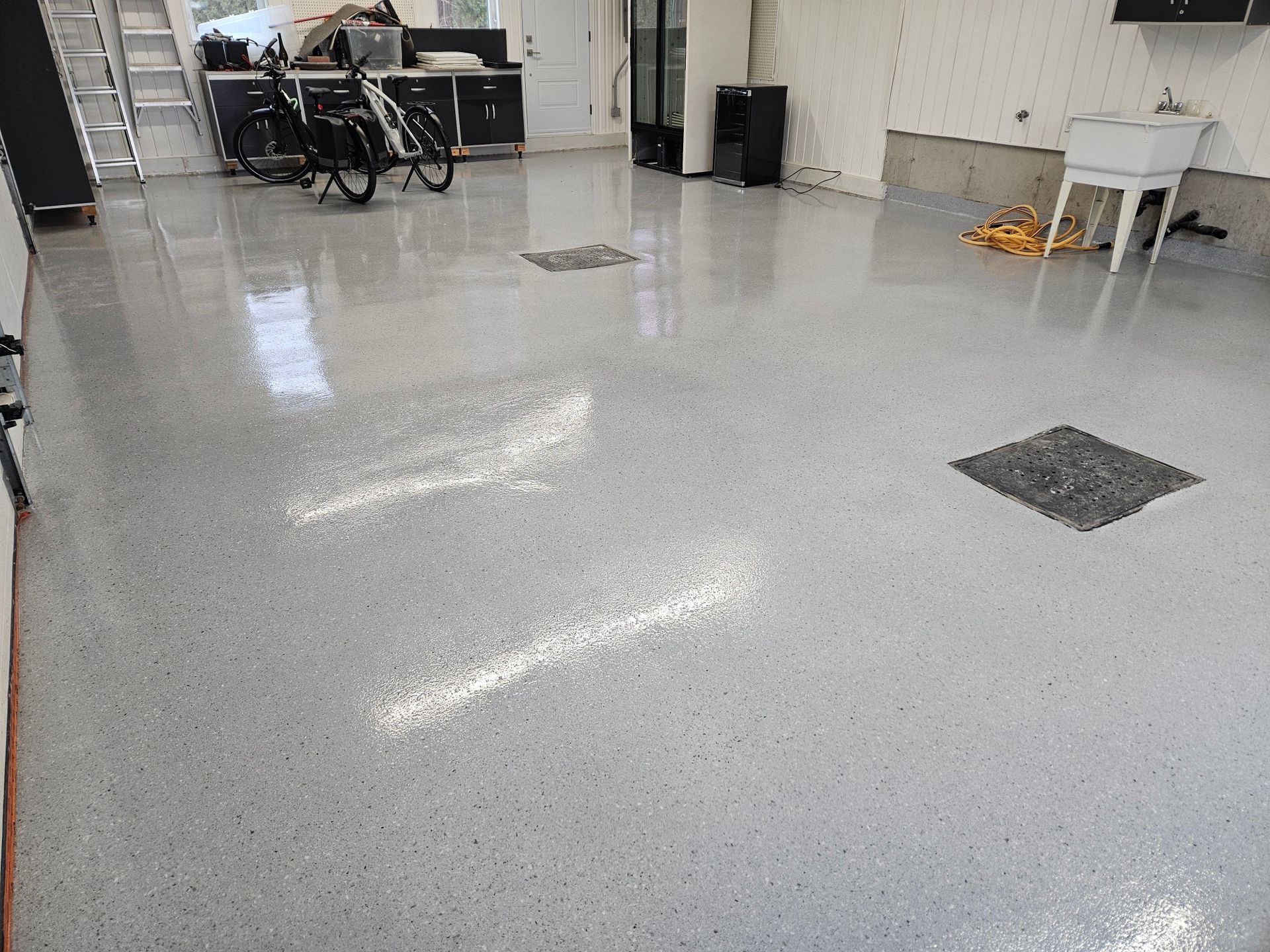 Garage with light gray speckled epoxy floor; a bicycle, cabinets, and a utility sink are visible.