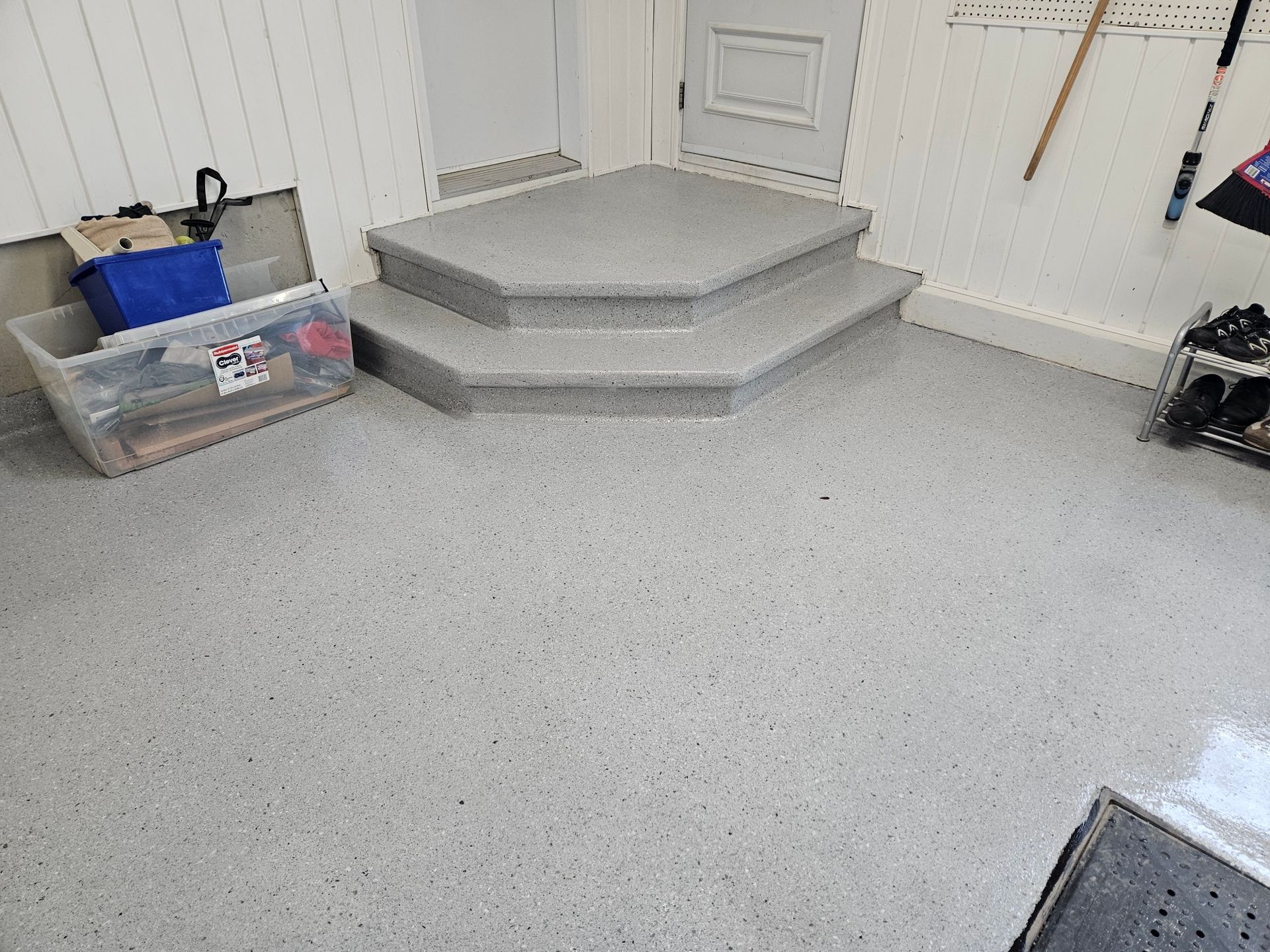 Gray speckled concrete garage floor and steps with a clear plastic bin and door.